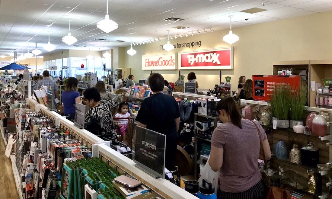 Shoppers wait in line at the checkout area of a HomeGoods and T.J.Maxx store, surrounded by shelves filled with home decor, kitchen items, and various household goods.