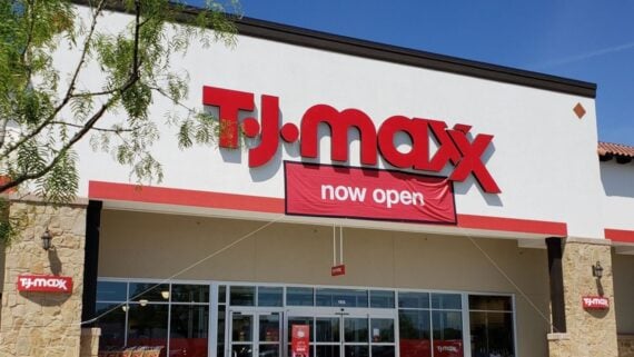 The front entrance of a TJ Maxx store with a large red sign and a banner underneath that reads "now open" on the white building facade.