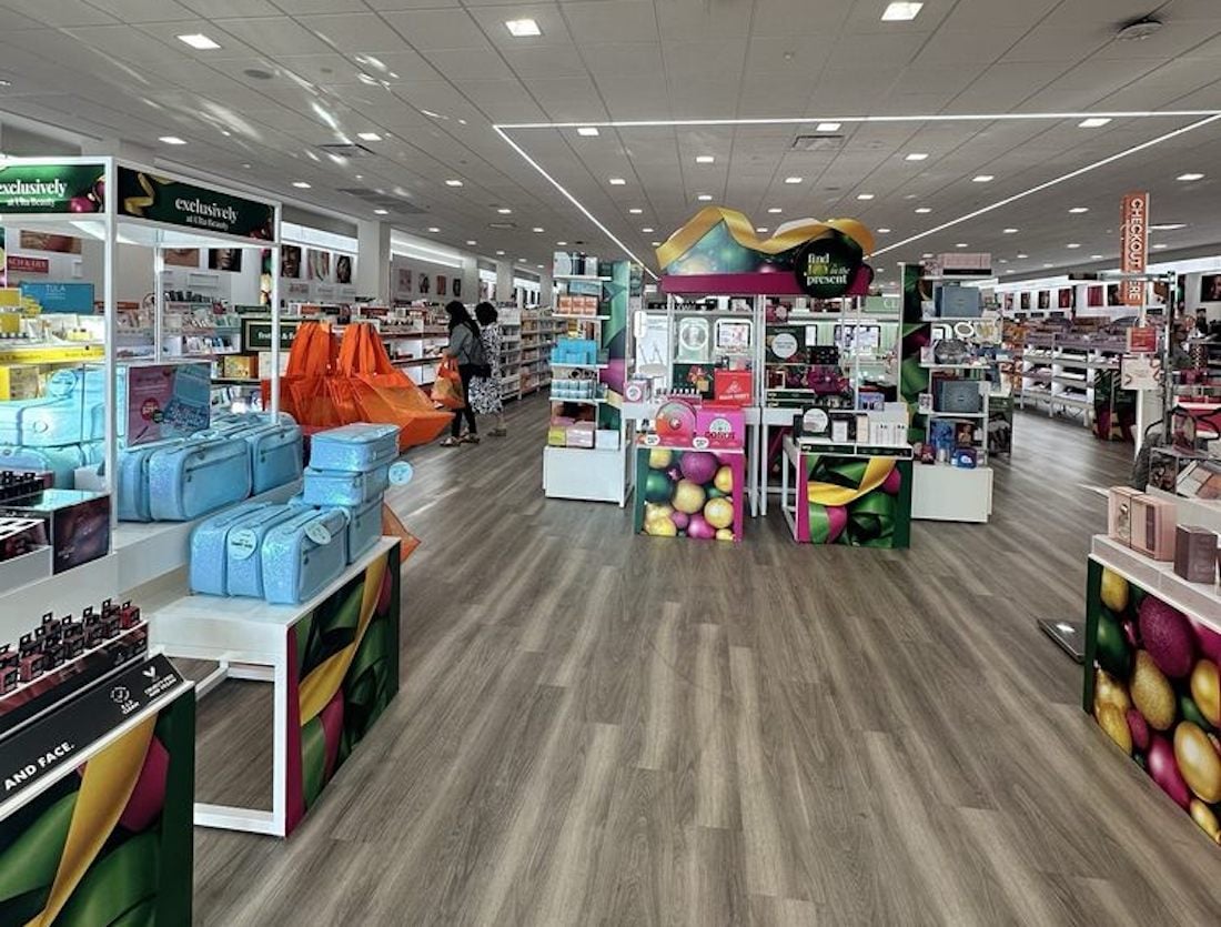 A spacious beauty store with colorful displays, various skincare and makeup products, travel bags, and shoppers browsing the aisles under bright lighting and a modern, clean interior.