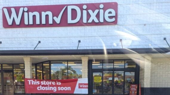 A Winn-Dixie grocery store with a large red sign above the entrance and a red banner below that reads, “This store is closing soon.” Yellow “Store Closing Sale!” signs are visible inside the windows.