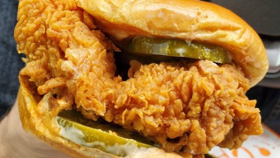 Close-up of a crispy fried chicken sandwich with pickles and sauce on a soft, shiny bun—perfect for celebrating National Fried Chicken Sandwich Day.