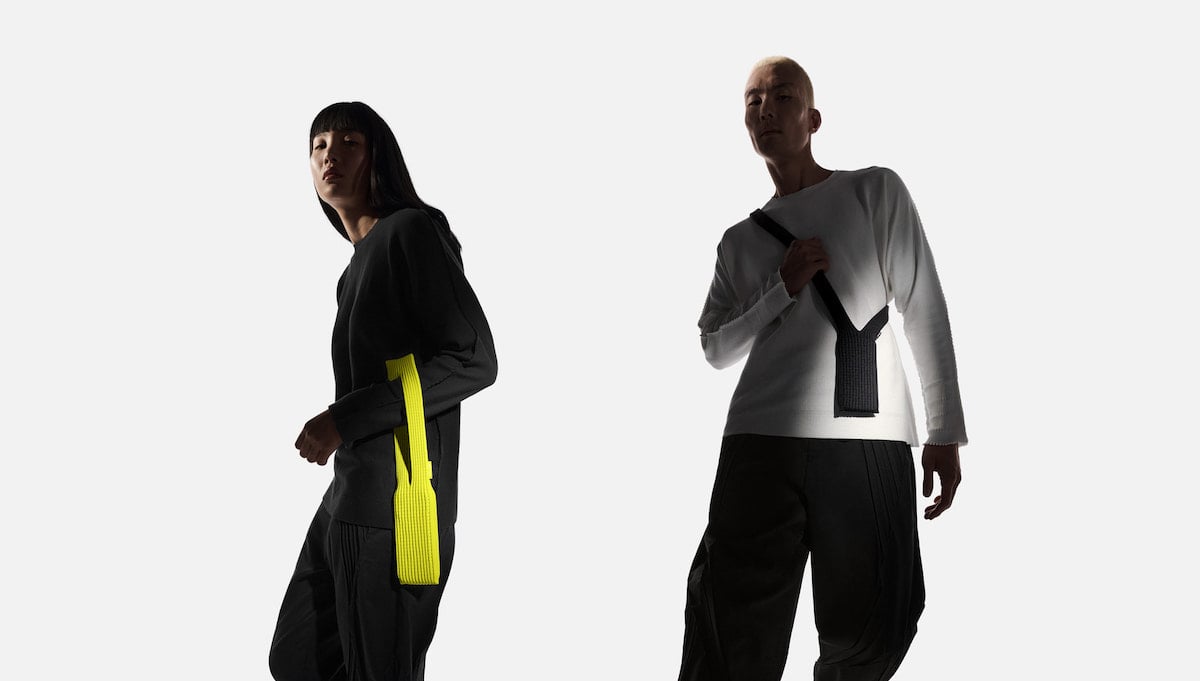Two models pose against a white background, one wearing a black outfit with a bright yellow textured bag, and the other in a white top with a black textured bag, both with modern, minimalist style.