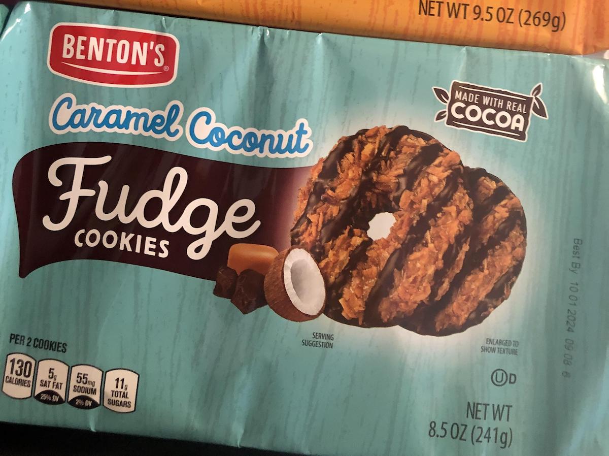 A package of Benton's Caramel Coconut Fudge Cookies is shown. The teal wrapper features images of caramel coconut cookies, chocolate, and a coconut, and highlights that the product is made with real cocoa.