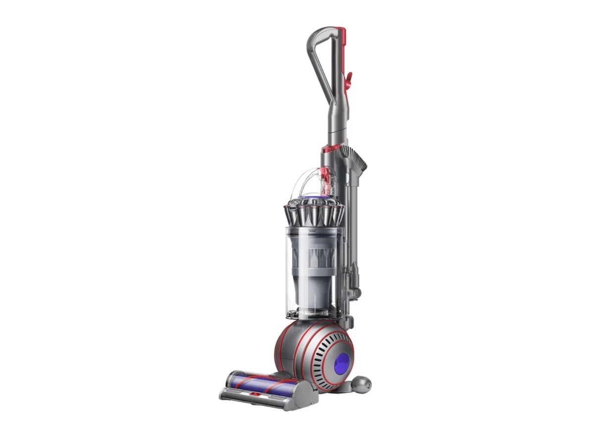 A modern upright vacuum cleaner with a clear dust canister, red and purple accents, and a large ball-shaped wheel for easy maneuverability, standing on a white background.