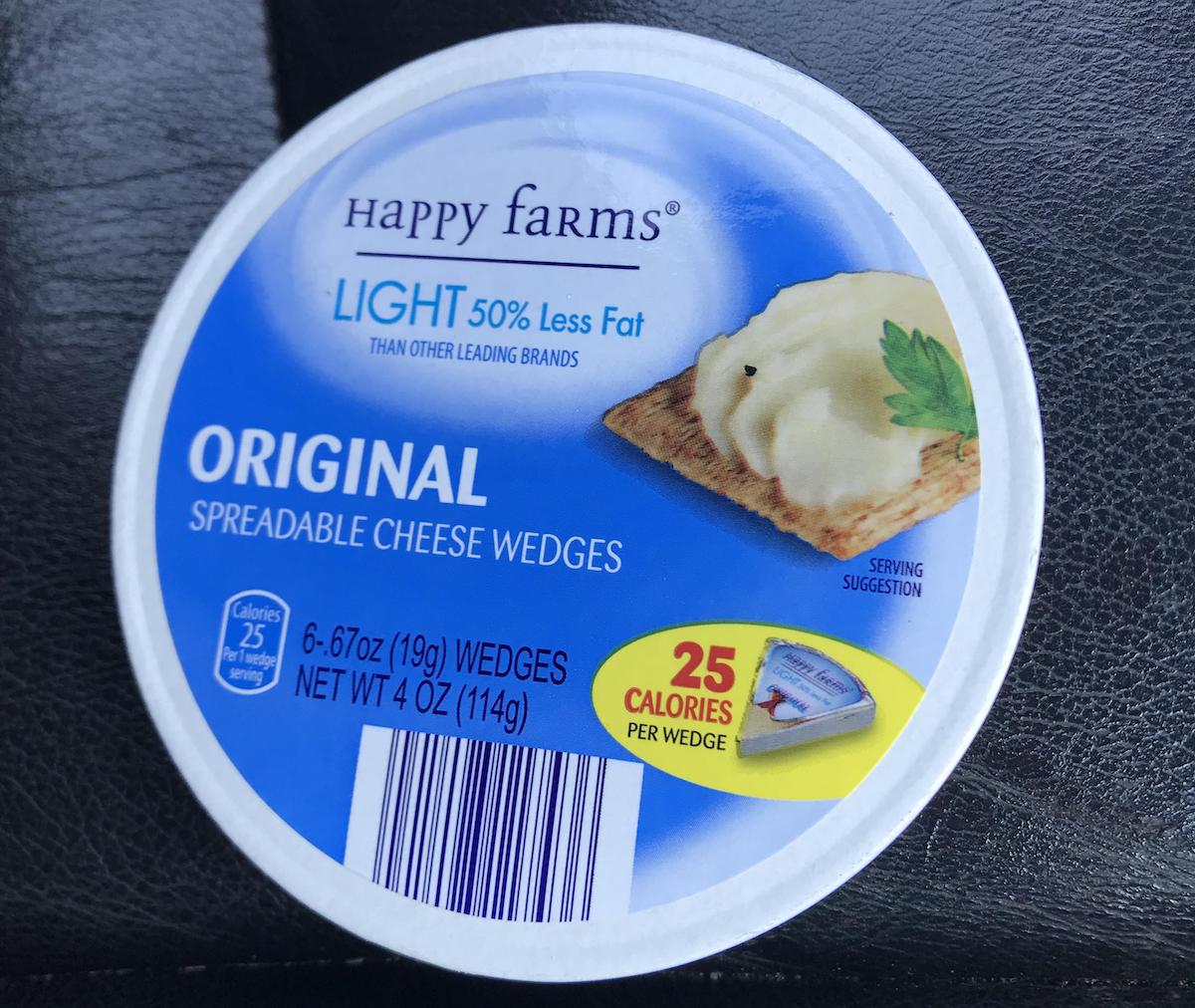 A round container of Happy Farms Light Original Spreadable Cheese Wedges, showing a cracker with cheese and a parsley leaf on the label. The packaging highlights 50% less fat and 25 calories per wedge.