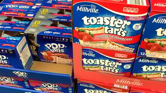 Boxes of Pop-Tarts and Millville Toaster Tarts, both strawberry flavored, are stacked side by side on store shelves. The packaging features images of the pastries with strawberry filling.