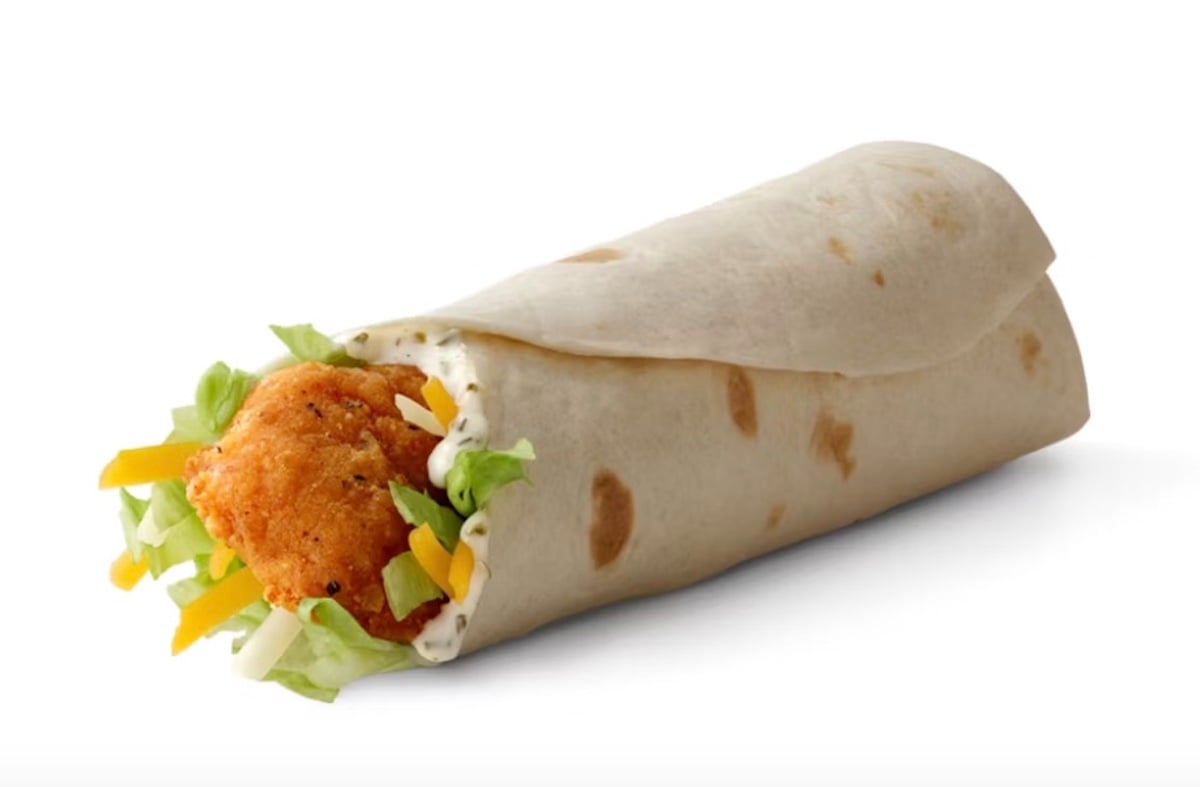 A flour tortilla wrap filled with a crispy breaded chicken fillet, shredded lettuce, and yellow cheese, against a plain white background.