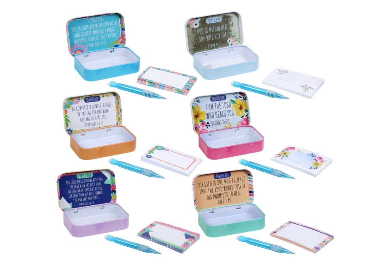 Six colorful tins, each with an inspirational quote inside, are paired with matching pens and notepads. The tins feature different colors and designs, displayed against a white background.