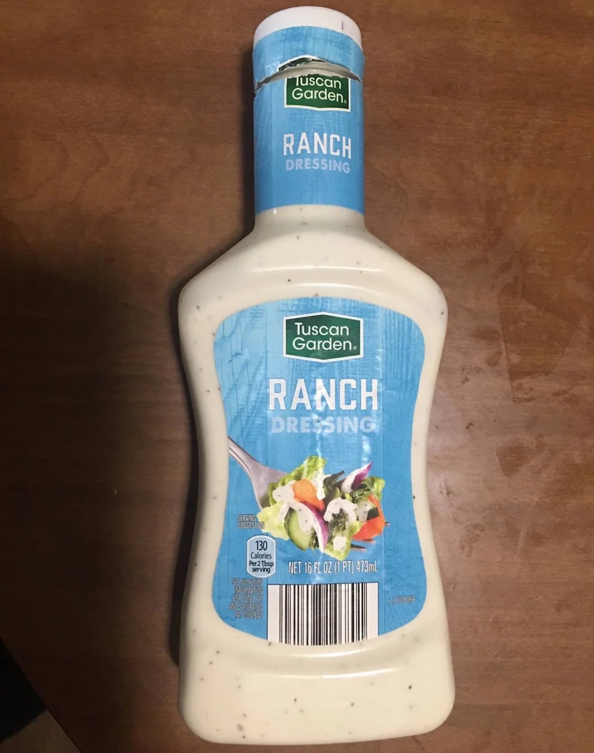 A bottle of Tuscan Garden Ranch Dressing with a blue label is placed on a wooden surface. The label shows an image of salad and states the bottle contains 16 fl oz (473 ml).