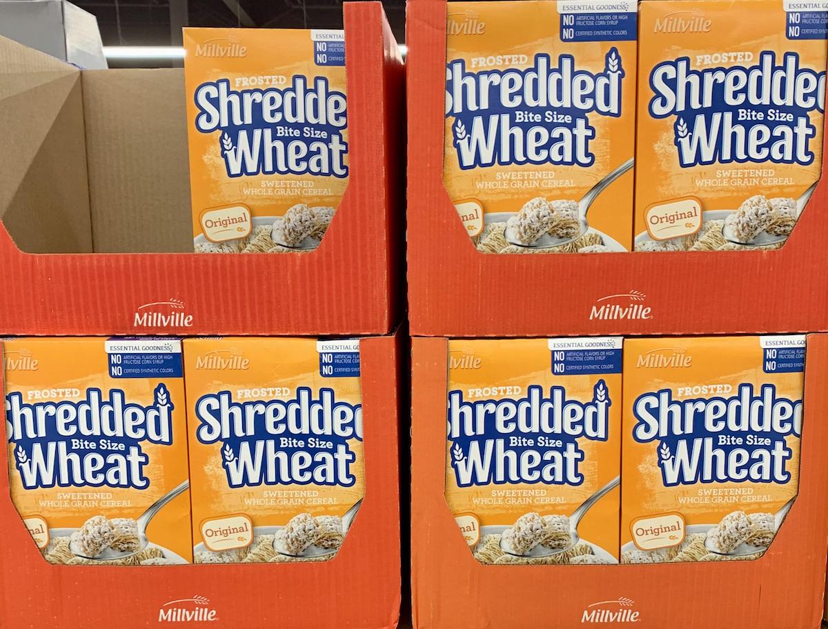 Four boxes of Millville Frosted Shredded Wheat Bite Size cereal are stacked on a store shelf, showing the front label with images of the cereal squares and product details.