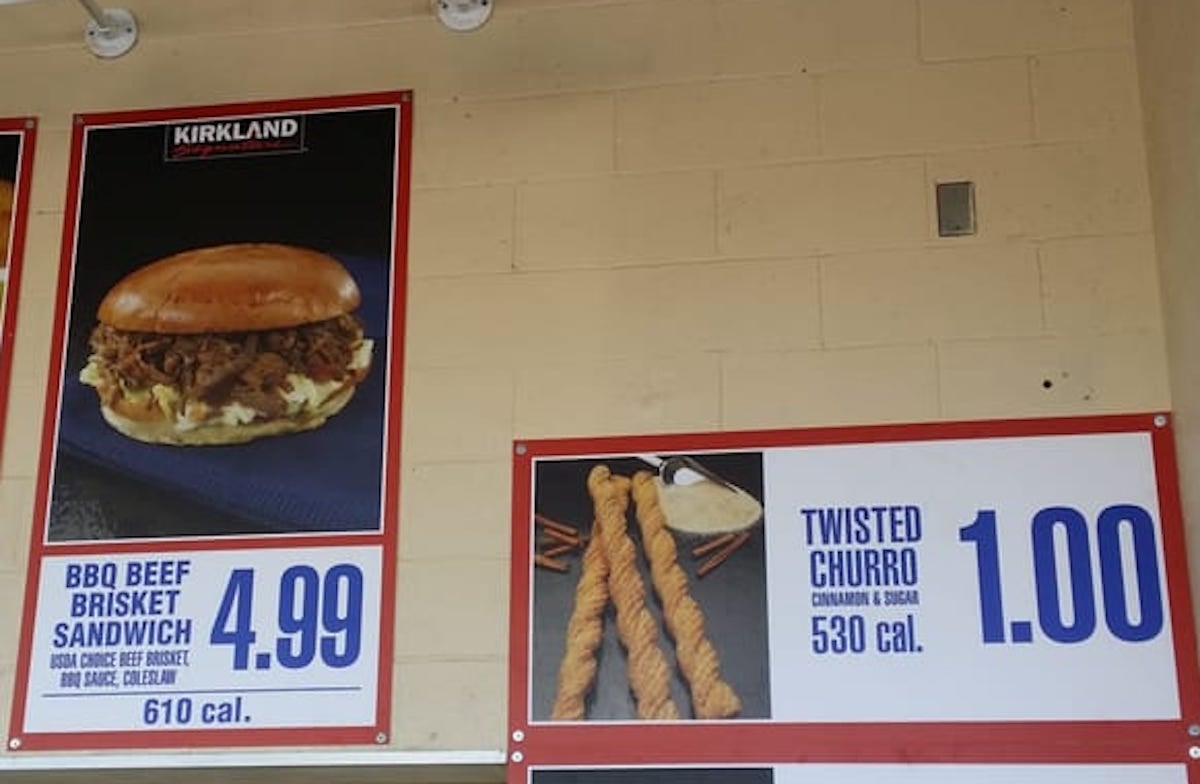 Two Costco food court menu signs: one shows a BBQ beef brisket sandwich for $4.99 with 610 calories; the other shows two twisted churros for $1.00 with 530 calories, with cinnamon sticks and sugar pictured.