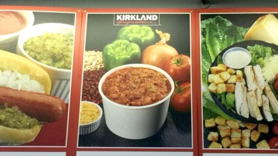 A poster displays a cup of chili surrounded by green bell peppers, an onion, beans, and shredded cheese, with "Kirkland Signature" branding above.