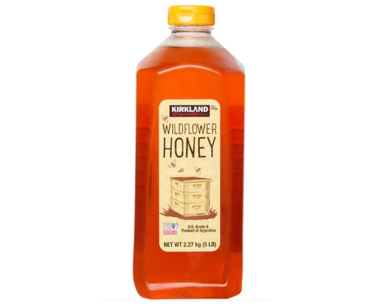 A plastic bottle of Kirkland Wildflower Honey with a yellow cap, featuring a label with a beehive illustration and information stating it is U.S. Grade A, product of Argentina, and weighs 2.27 kg (5 lb).