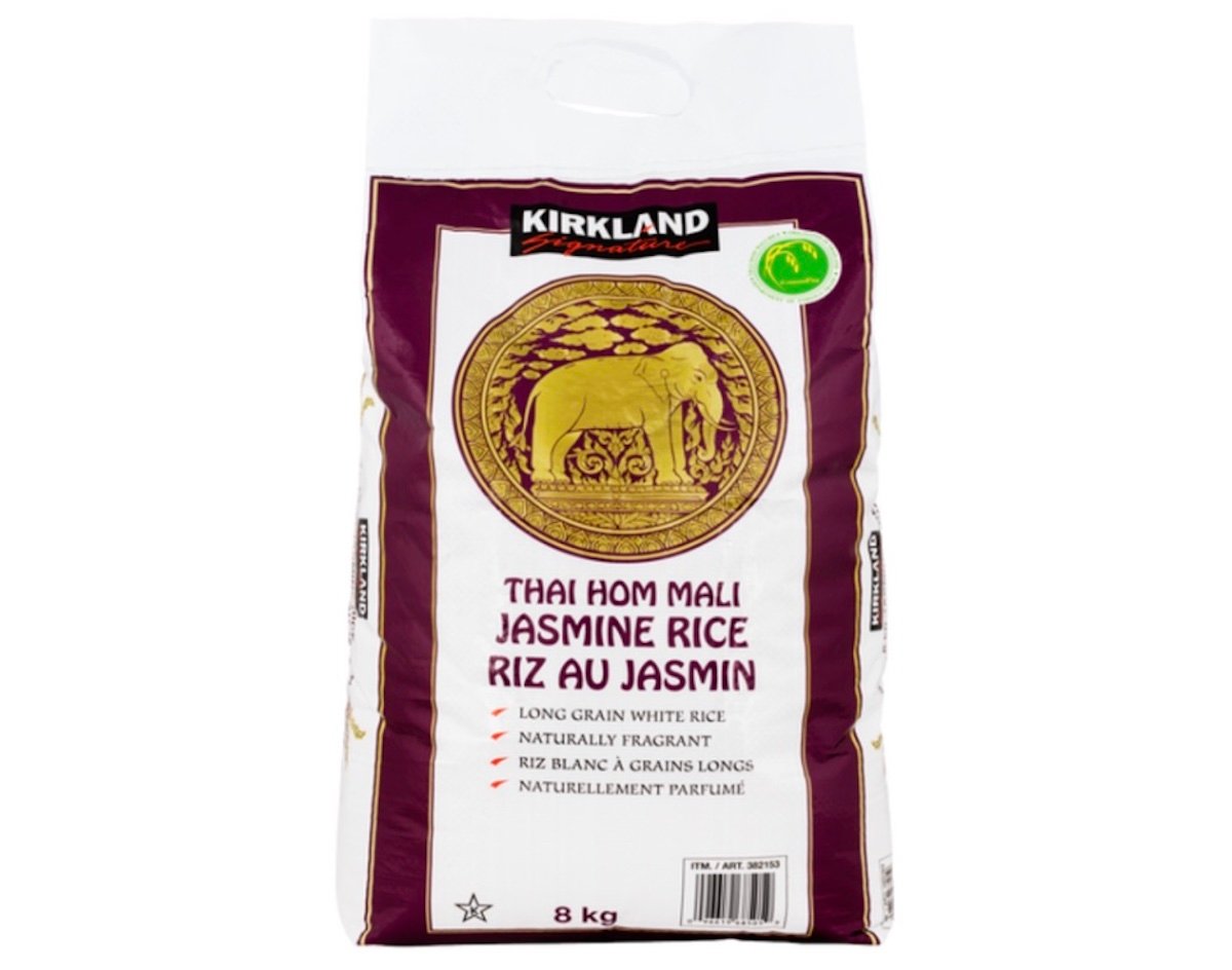 A white and purple 8 kg bag of Kirkland Signature Thai Hom Mali Jasmine Rice featuring a gold elephant emblem and text in English and French about the rice's fragrance and long grains.