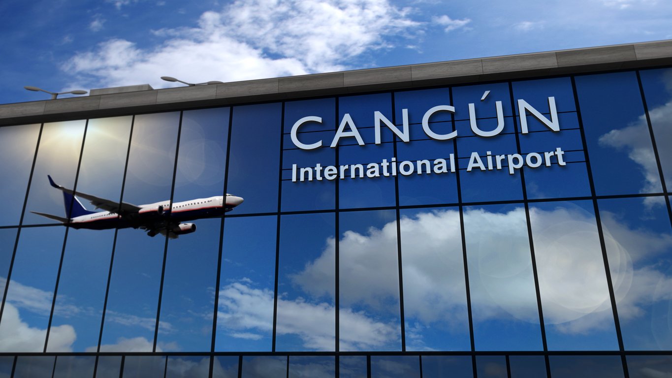 A glass building with the words "CANCÚN International Airport" reflects the sky and clouds, while an airplane flies nearby.