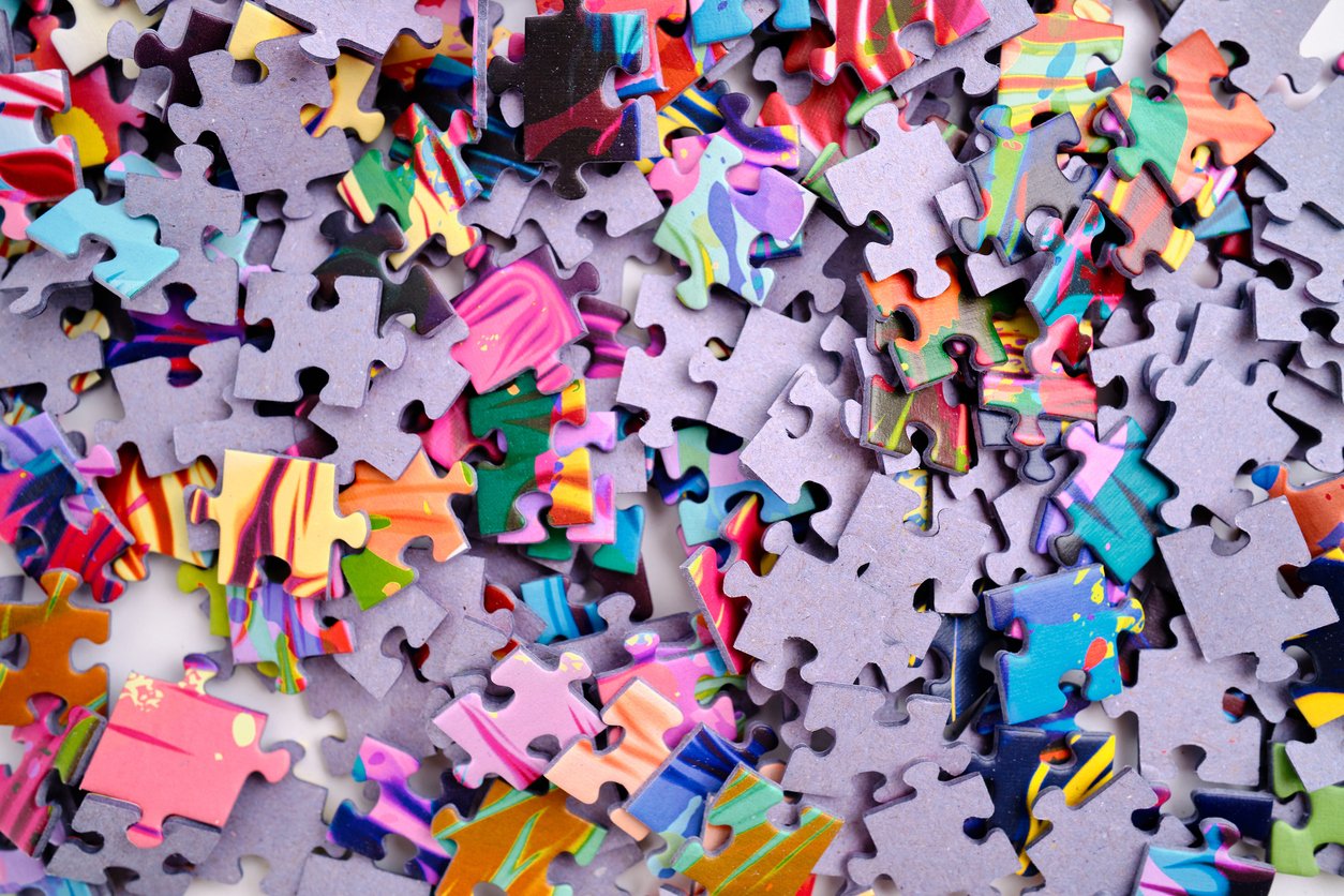 A close-up of scattered jigsaw puzzle pieces, featuring a mix of colorful and vibrant abstract patterns on one side, with the reverse side being plain and light purple.