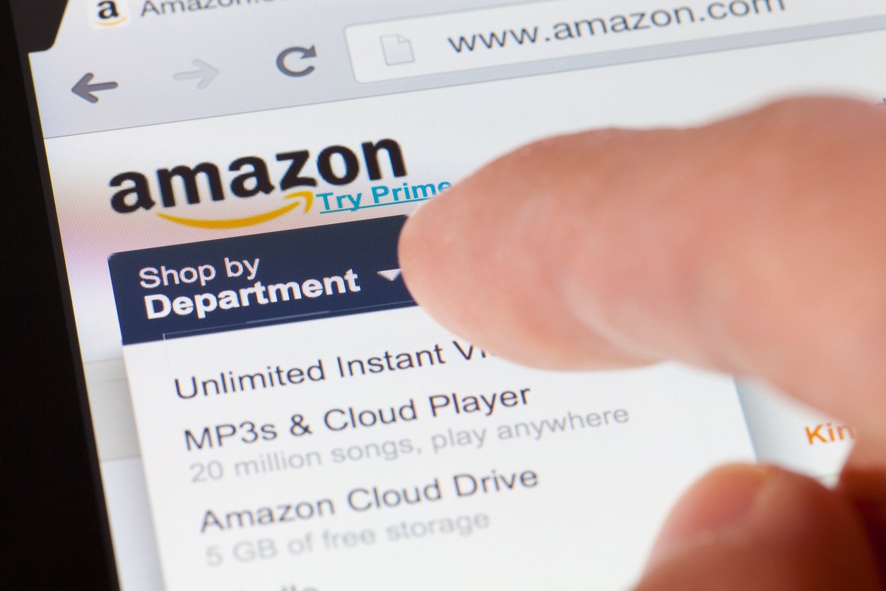 A close-up of a person using a touchscreen device to browse the "Shop by Department" dropdown menu on the Amazon website, with options like "Unlimited Instant Video" and "MP3s & Cloud Player" visible.