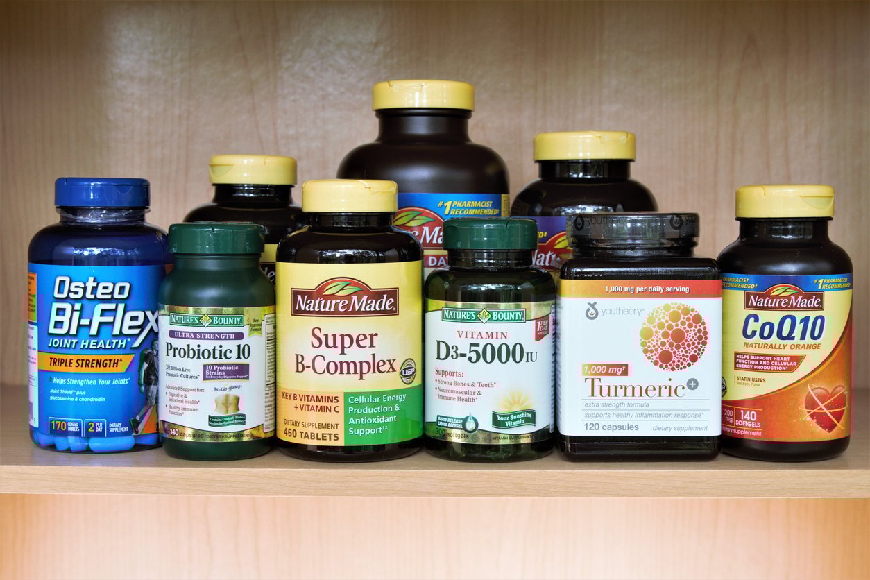 A shelf with various supplement bottles, including Osteo Bi-Flex, Probiotic 10, Nature Made Super B-Complex, Vitamin D3, CoQ10, Nature's Bounty Turmeric, and other vitamin bottles.