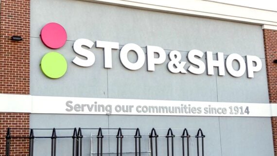 The image shows the exterior sign of a Stop & Shop store, featuring the store’s name in large white letters and the slogan “Serving our communities since 1914” beneath it. Two colored circles are on the left of the sign.