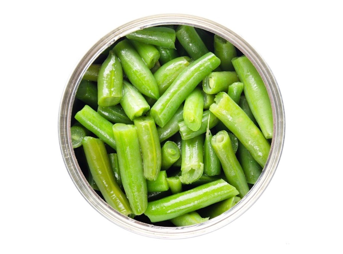 A top-down view of a can filled with cut green beans, shown against a white background. The beans are bright green and neatly packed inside the circular metal can.