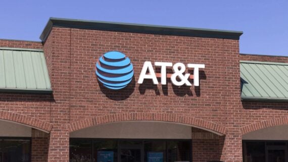 A brick building with a green roof features the AT&T logo and name in white letters on its exterior, under a clear blue sky.
