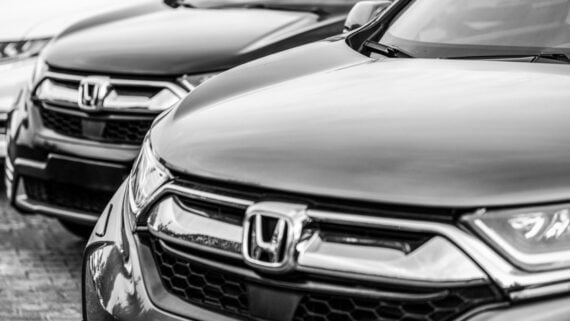 Black and white close-up photo of the front ends of several Honda vehicles parked in a row, focusing on the grilles and Honda emblems.