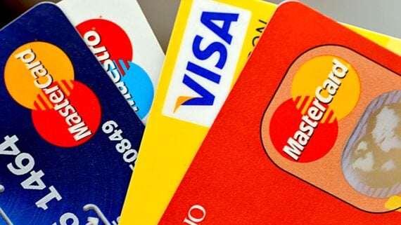 Close-up of three Mastercard credit cards and one Visa credit card, overlapping each other in a fan arrangement, showing their logos and partial card numbers.