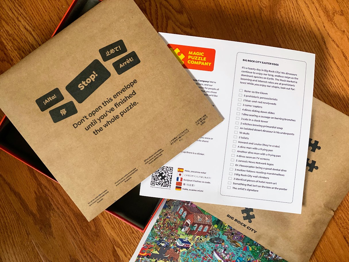 A partially opened puzzle box reveals an envelope labeled, "Don't open this envelope until you've finished the whole puzzle," along with a checklist titled "Big Rock City Easter Eggs" and part of a colorful puzzle on a wooden floor.
