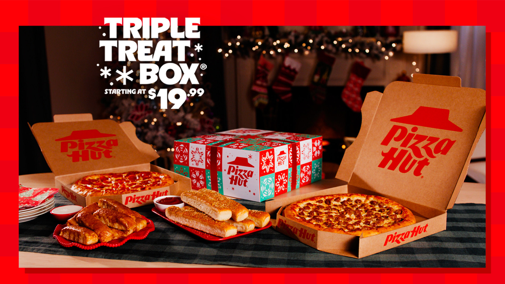 A festive Pizza Hut Triple Treat Box with two pizzas, breadsticks, and cinnamon rolls sits on a table, showcasing holiday-themed packaging and Christmas decorations. Discover this new fast-food menu offer starting at $19.99.