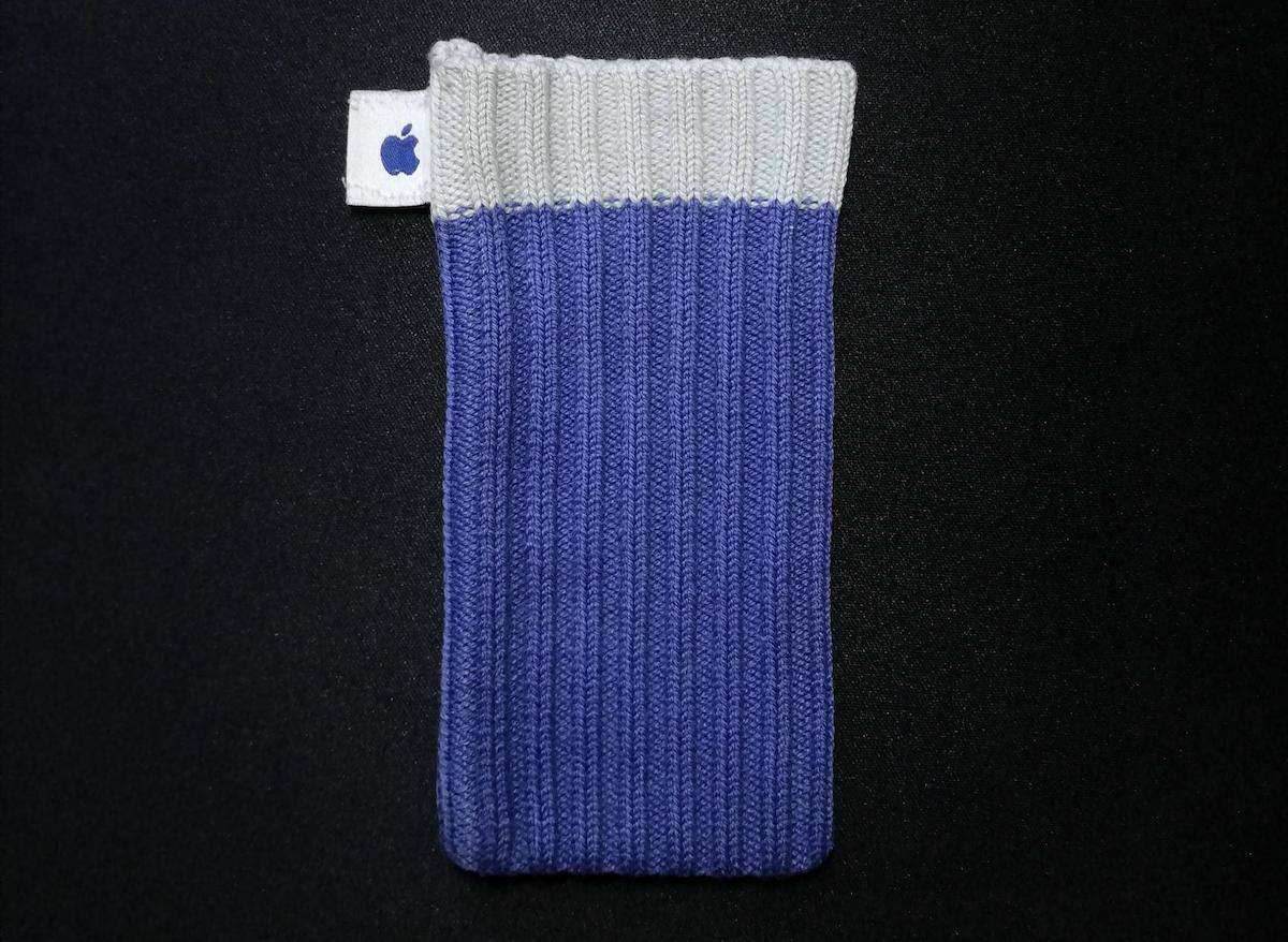 A ribbed knit fabric pouch with a light gray top and purple body, featuring a small white tag with a blue Apple logo on the left, displayed on a black background.