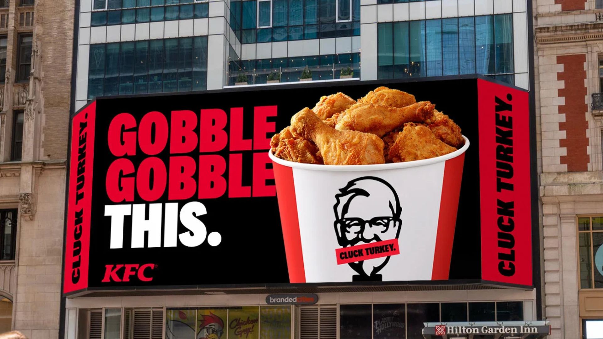 A large KFC billboard displays a bucket of fried chicken with the words "GOBBLE GOBBLE THIS." in bold text. The Colonel Sanders logo has "CLUCK TURKEY" over his mouth, and "CLUCK TURKEY" is repeated on the edges.