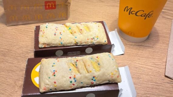 Two McDonald's dessert pies with sprinkle topping sit in open boxes on a wooden table next to a McCafé cup and a paper McDonald's bag.