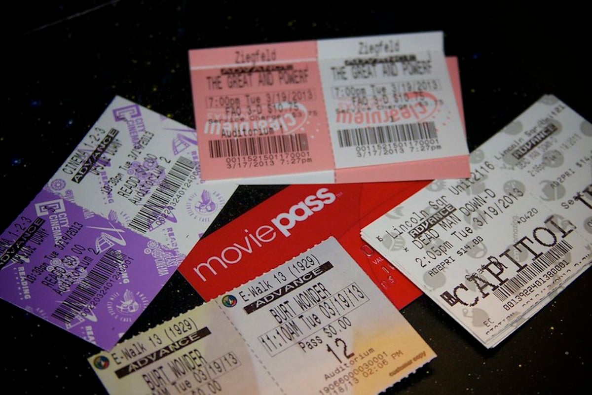 A close-up of five assorted movie tickets and a red MoviePass card arranged on a dark surface with colorful speckles. The tickets show various movie titles, dates, and theater locations.