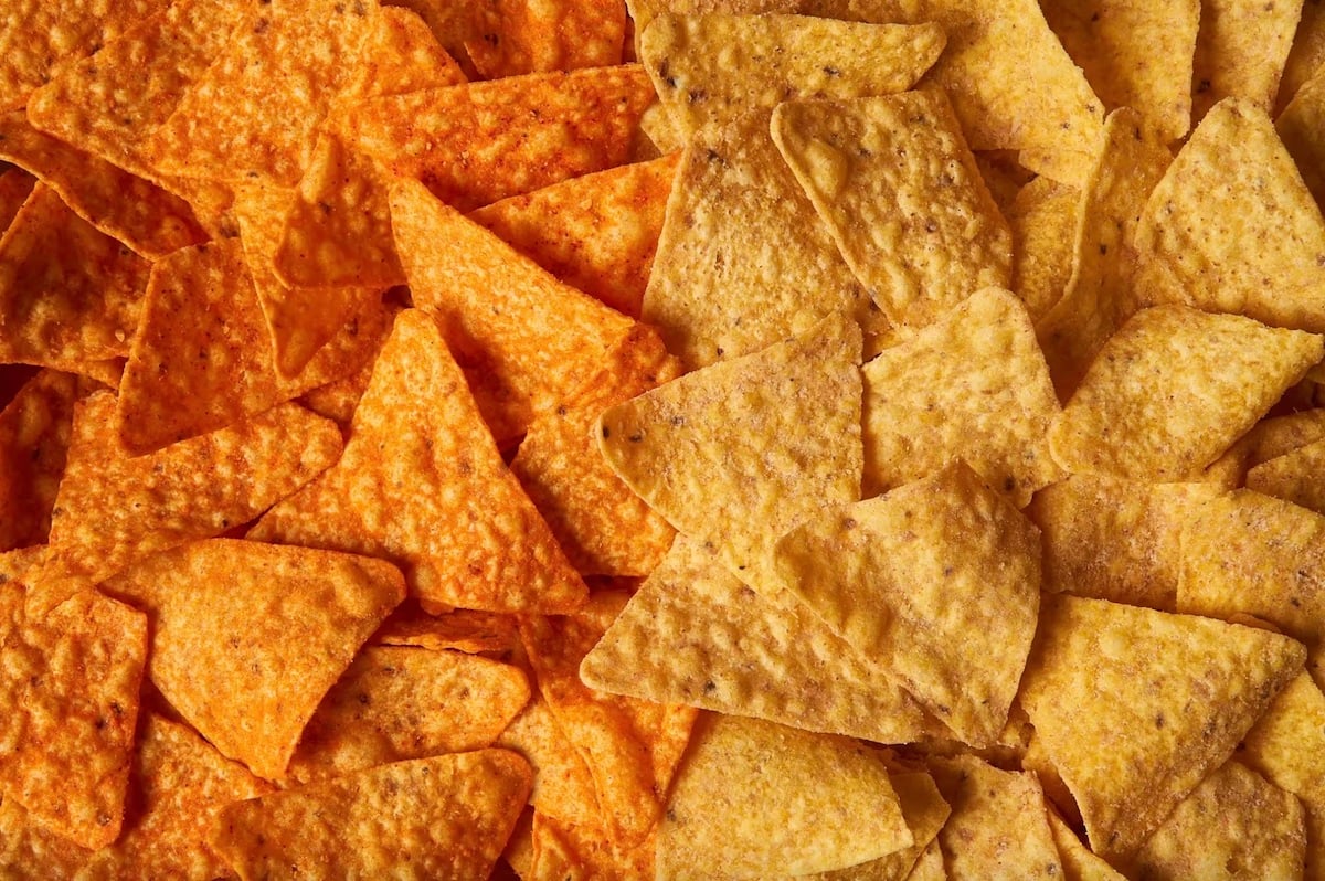 A close-up view of two types of tortilla chips: nacho cheese flavored on the left, which are orange, and plain yellow corn tortilla chips on the right. The chips are arranged side by side, filling the entire frame.