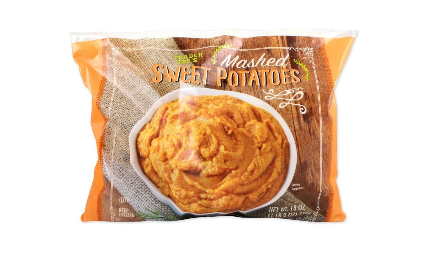 A bag of Trader Joe’s Mashed Sweet Potatoes, showing an image of mashed sweet potatoes in a white bowl on a rustic wooden surface, with the packaging labeled “Keep Frozen” and “Net Wt. 18 oz.”