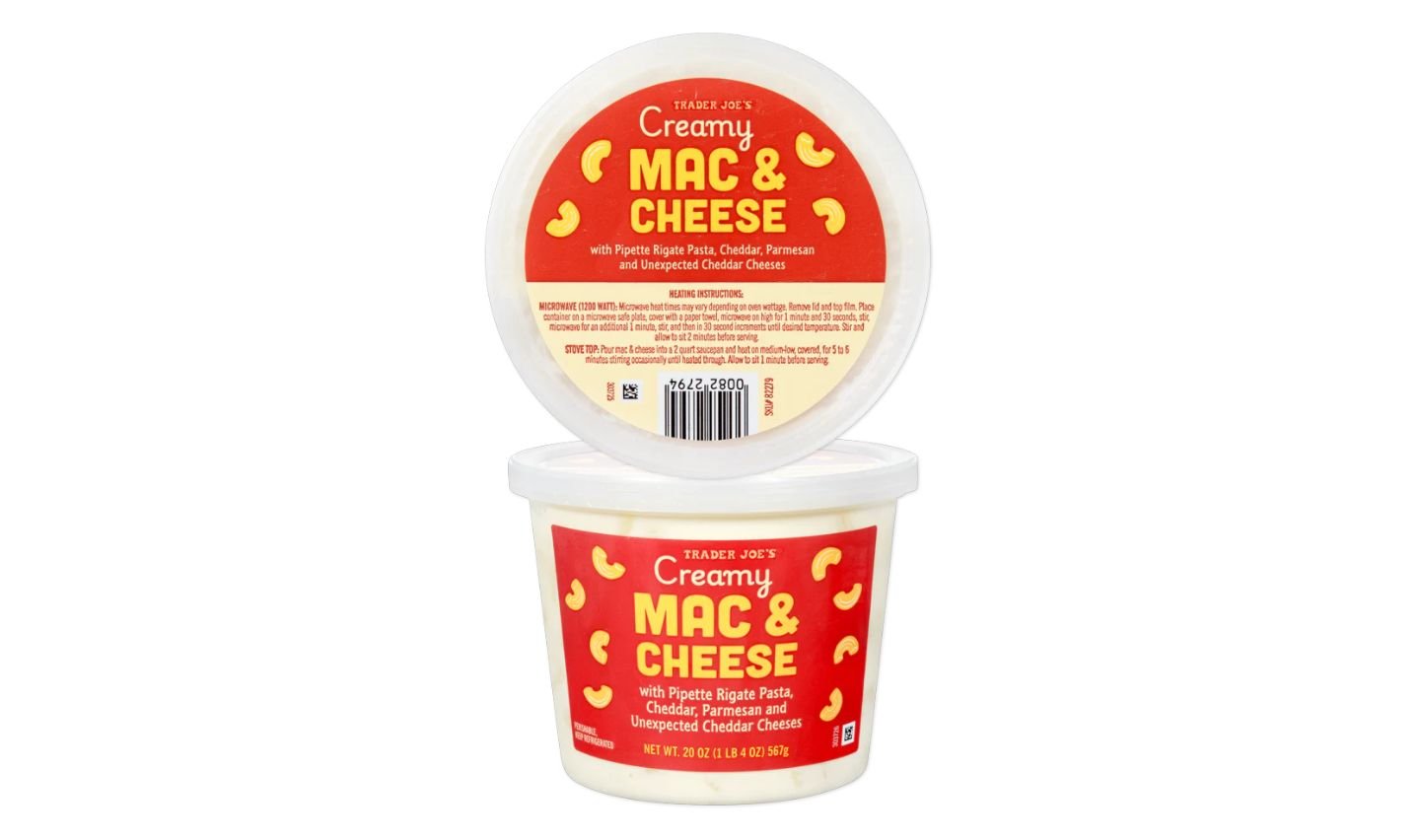 A tub of Trader Joe’s Creamy Mac & Cheese with a red label displaying the product name and ingredients, including rigate pasta, cheddar, parmesan, and unexpected cheddar cheese.