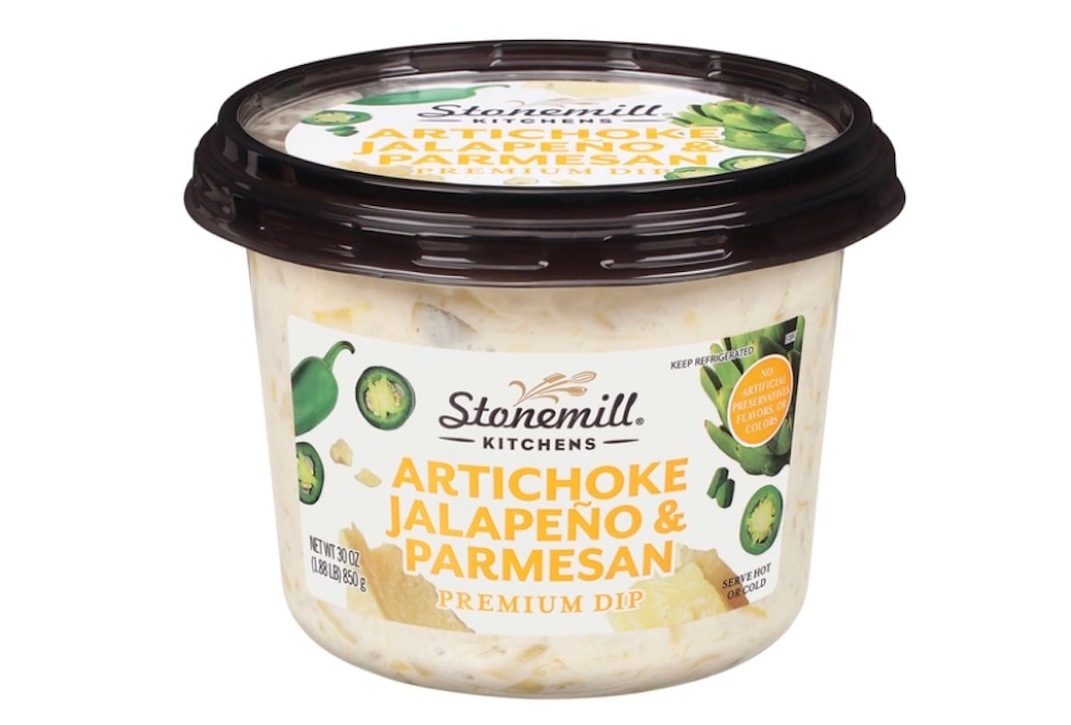 A plastic container of Stonemill Kitchens Artichoke Jalapeño & Parmesan Premium Dip, featuring images of artichoke and jalapeño slices on the label, with a dark brown lid.
