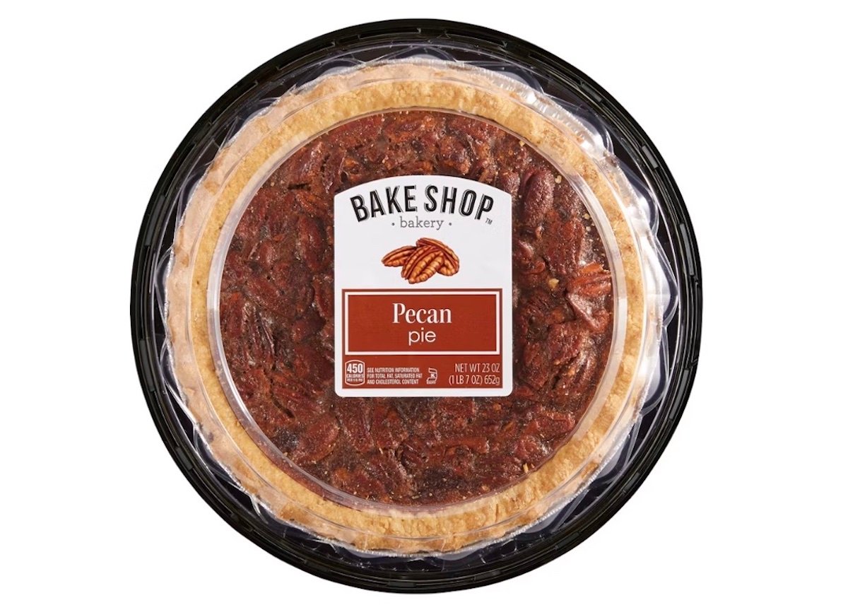 A whole pecan pie in a black plastic tray covered with clear plastic wrap. The label reads "Bake Shop Bakery Pecan Pie" and displays a picture of a pecan. The pie has a golden crust and a pecan topping.
