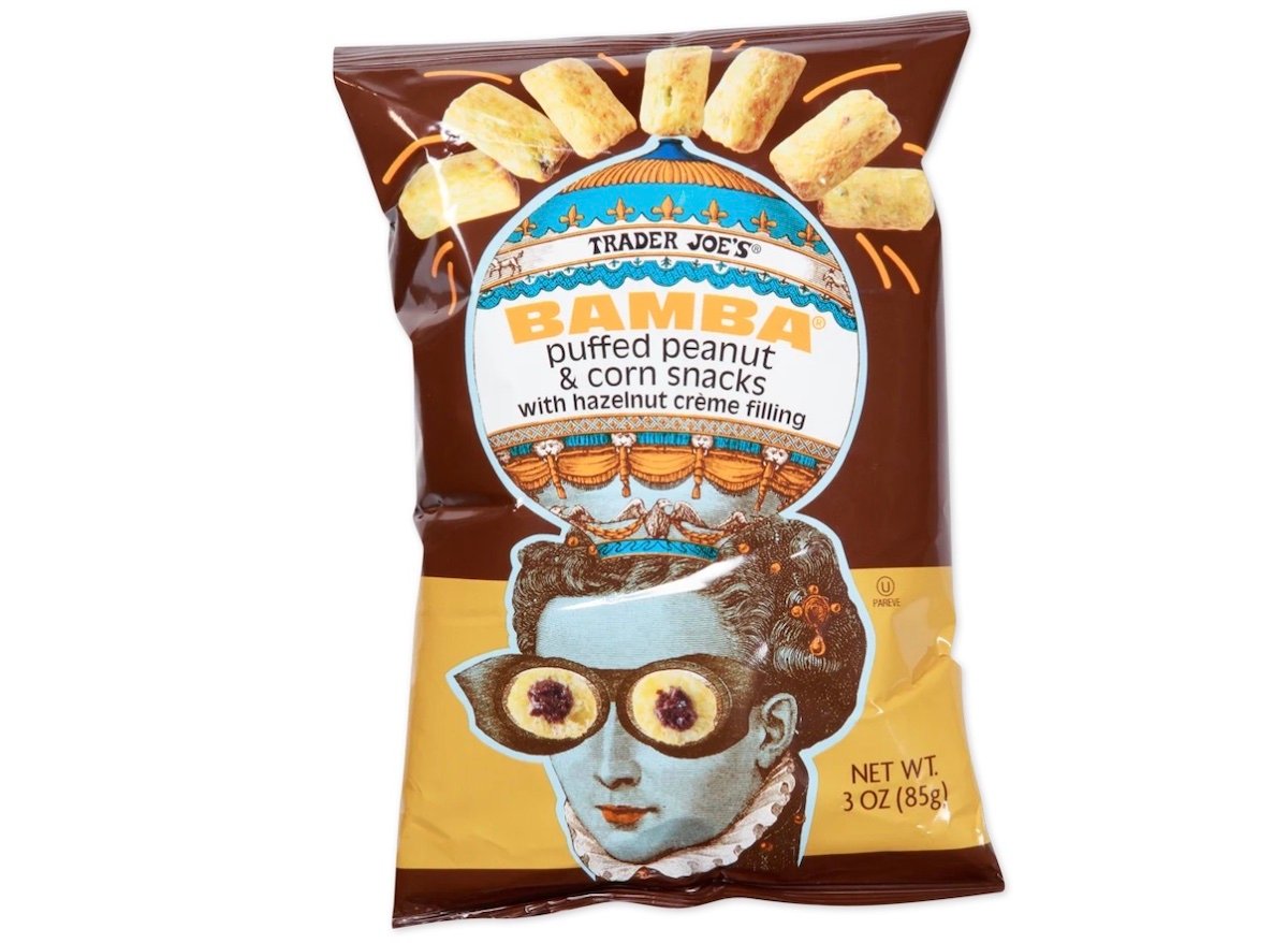 A bag of Trader Joe’s Bamba Puffed Peanut & Corn Snacks with Hazelnut Crème Filling. The packaging features whimsical art of a person with snacks for glasses and a crown, and bright, playful designs. Net weight: 3 oz (85g).