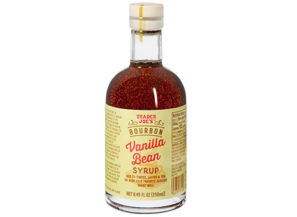 A bottle of Trader Joe's Bourbon Vanilla Bean Syrup with a clear glass body, gold cap, and a cream-colored label featuring red and brown text. The syrup inside appears dark brown.