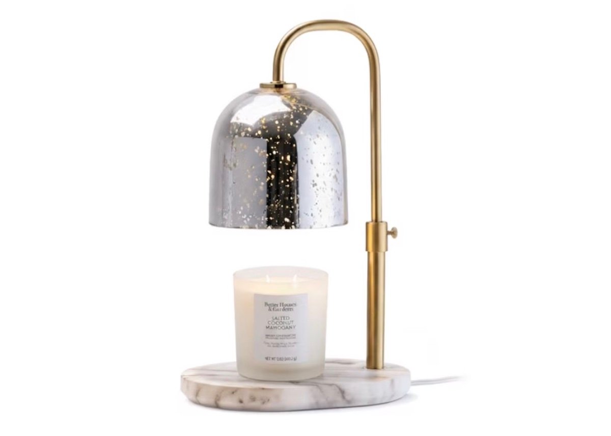 A candle warmer lamp with a gold metallic frame, a dome-shaped reflective shade, and a marble base, holding a lit white candle underneath.