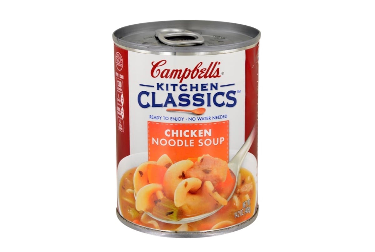 A can of Campbell’s Kitchen Classics Chicken Noodle Soup with a red and blue label, featuring an image of soup with noodles, carrots, and chicken in a white bowl. The can is 14.2 ounces.