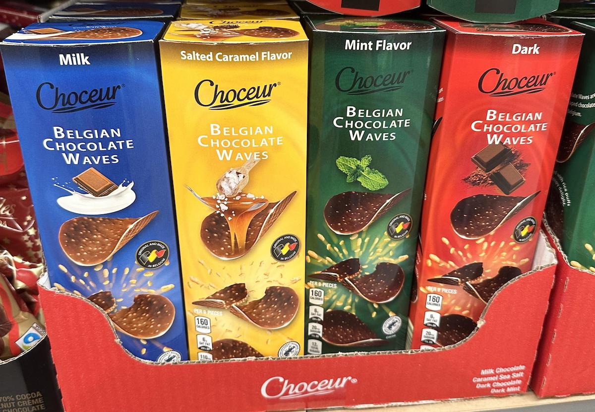 Four boxes of Choceur Belgian Chocolate Waves in a display: milk, salted caramel, mint, and dark flavors. Each box shows chocolate pieces with corresponding ingredients on colorful backgrounds.