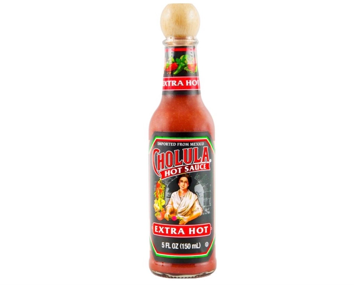 A 5 fl oz (150 ml) bottle of Cholula Extra Hot Sauce with a wooden cap and a colorful label featuring a woman, peppers, and "Imported from Mexico" text above the Cholula logo.