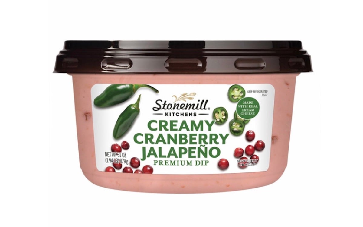 A tub of Stonemill Kitchens Creamy Cranberry Jalapeño Premium Dip, featuring images of cranberries and jalapeños on the label, with a black lid and a white background.