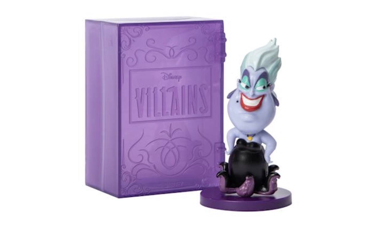 A figurine of Ursula from Disney's "The Little Mermaid" stands in front of a purple Disney Villains box designed to look like a book. Ursula has light blue hair, purple skin, and a mischievous grin.
