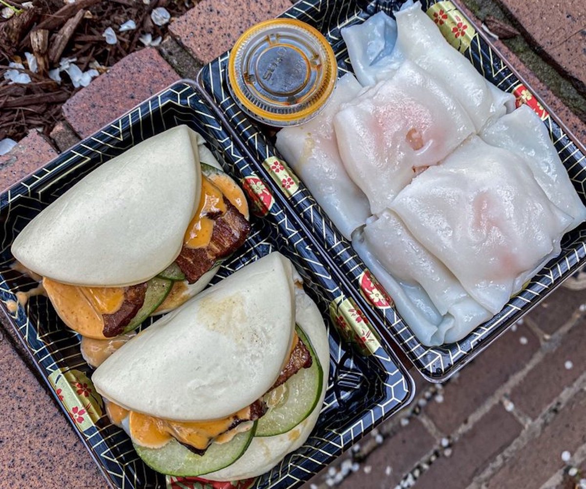Two black trays showcase dishes from under-the-radar restaurants: three steamed bao buns with meat, cucumber, and orange sauce, alongside translucent rice noodle rolls with a small container of dipping sauce.