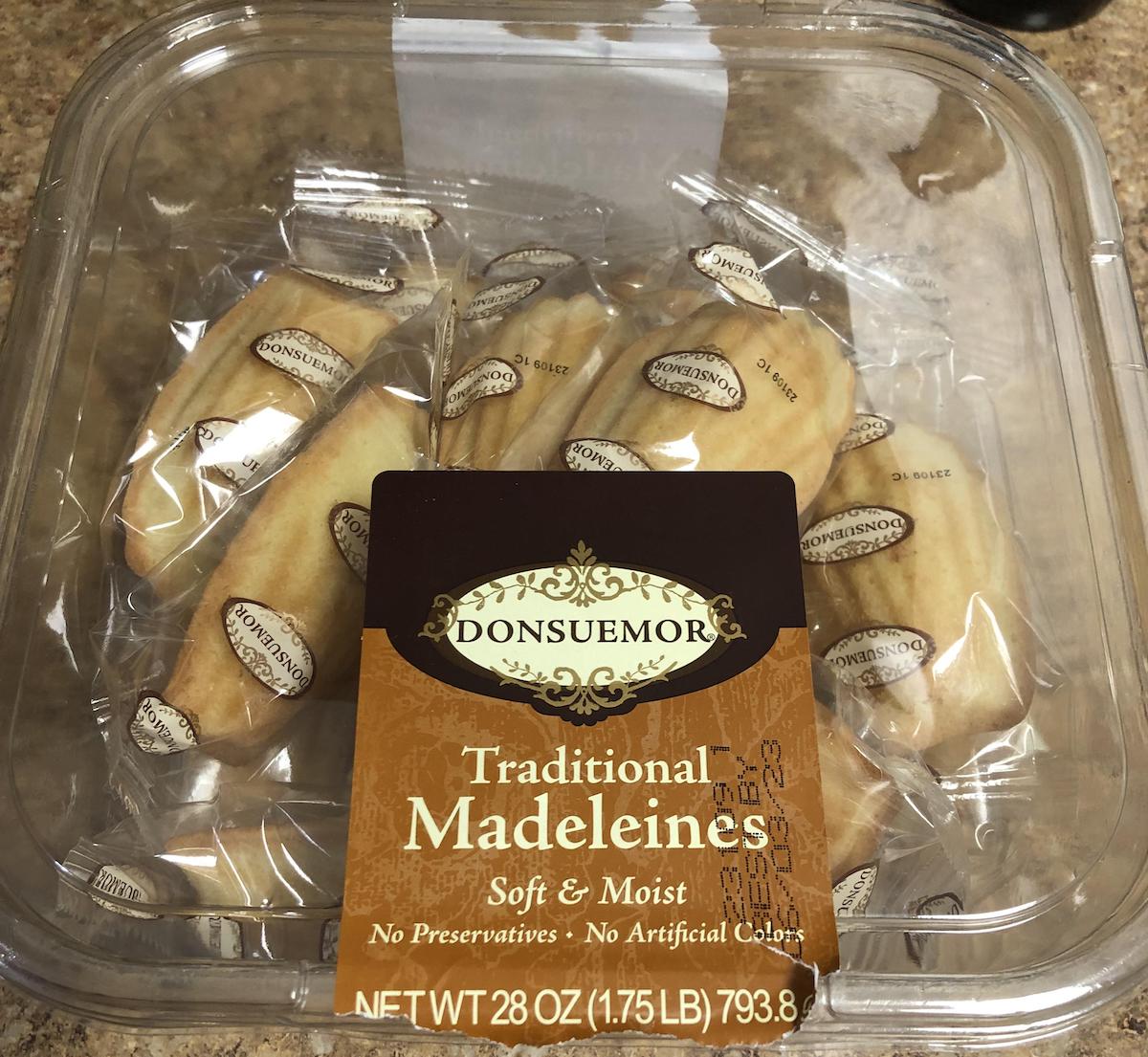 A clear plastic container holds individually wrapped Donsuemor traditional madeleines. The label reads, "Traditional Madeleines: Soft & Moist, No Preservatives, No Artificial Colors, 28 oz (1.75 lb) 793.8 g.