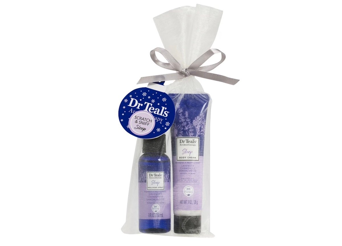 A gift bag containing two Dr Teal's Sleep products: a spray bottle and a tube of body cream. The bag is tied with a gray ribbon and has a blue tag that says “Dr Teal's Soak & Sleep Shop.”