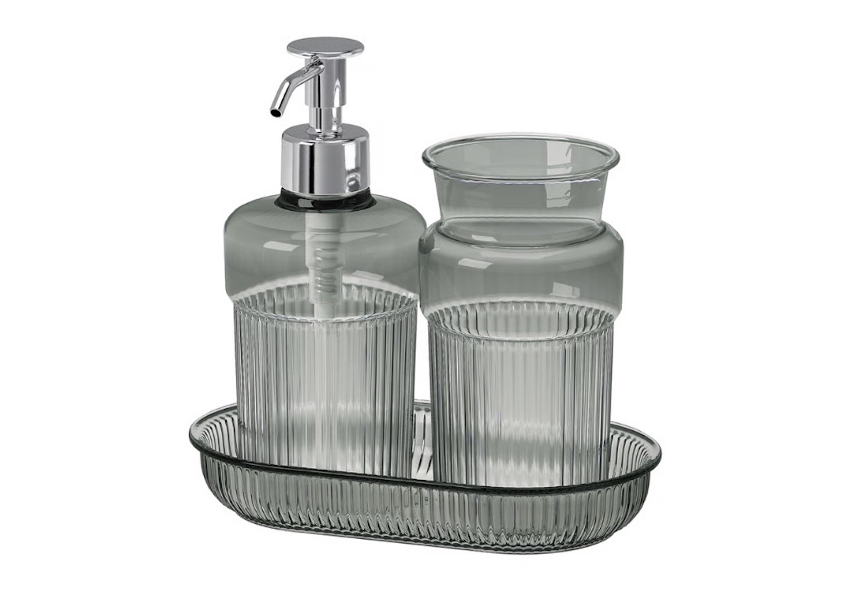 A set of clear, ribbed glass bathroom accessories on a matching tray, including a soap dispenser with a silver pump and a tumbler.